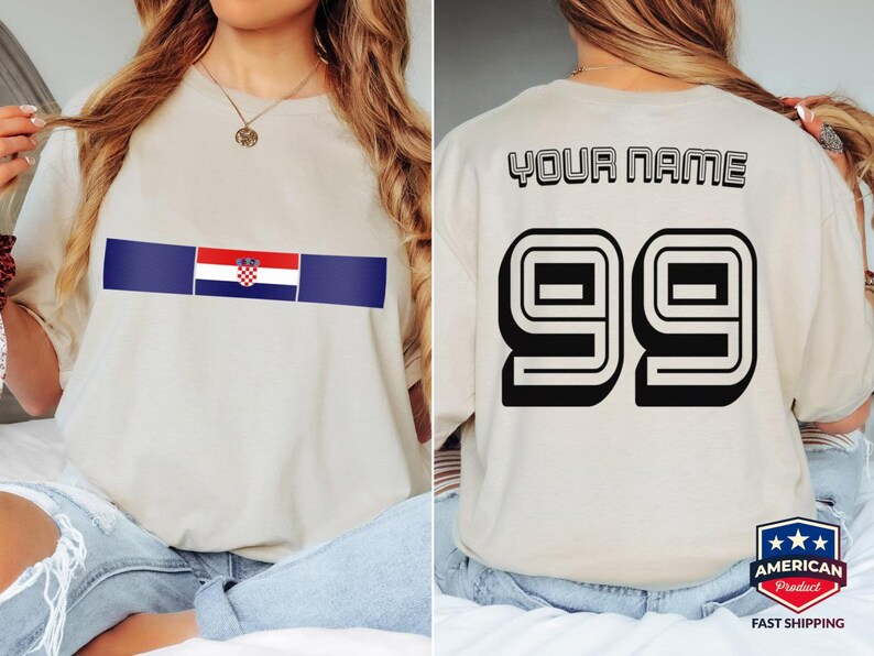 May include: A beige t-shirt featuring a horizontal stripe with the Croatian flag on the front. The back displays the text YOUR NAME in a black outlined font above the large black outlined number 99, styled like a sports jersey design.