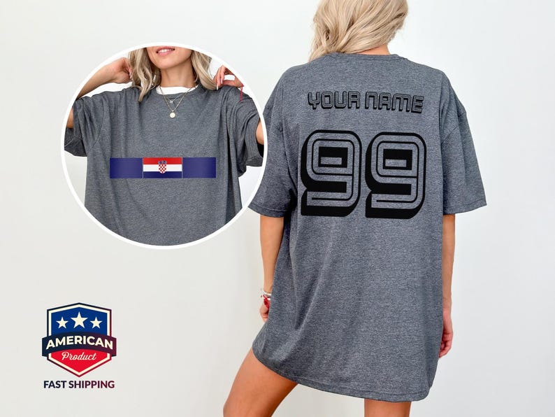May include: A dark gray t-shirt featuring a circular inset showing the front with a horizontal Croatian flag graphic. The back of the shirt displays the text YOUR NAME in black block letters above the large black outlined number 99.