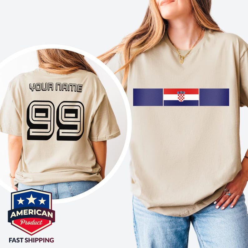May include: A beige short-sleeved t-shirt featuring a horizontal stripe with the Croatian flag in the center. The back of the shirt displays the text YOUR NAME above the large black number 99 in a bold, block-style font with a white outline.