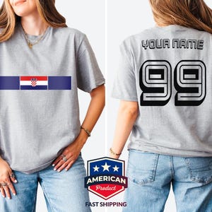 May include: A heather gray short-sleeve t-shirt featuring the Croatian flag centered on the chest. The back of the shirt displays the text YOUR NAME in black block letters above the large black outlined number 99 in a bold athletic font.