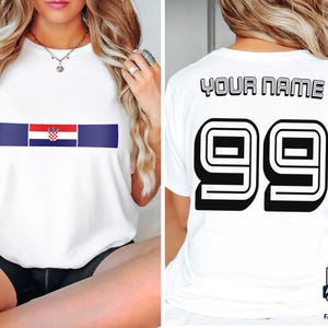 May include: A white short-sleeved t-shirt featuring a horizontal stripe with the Croatian flag on the front. The back of the shirt displays the text YOUR NAME in black block letters above the large black outlined number 99.