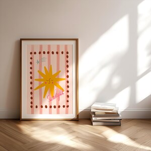 Peut inclure: Une affiche encadrée avec une illustration de soleil jaune souriant et le mot "Sunlight" en rose. Le fond présente des rayures roses et une bordure pointillée. Le cadre est de couleur marron clair.