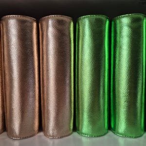 Könnte beinhalten: Reihe zylindrischer Objekte mit strukturierter, metallischer Oberfläche. Die Farben reichen von Bronze bis Grün. Die Objekte scheinen aus einem glänzenden, möglicherweise lederartigen Material zu bestehen.