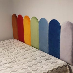 Può includere: Una testiera composta da sette pannelli verticali ad arco rivestiti in tessuto di velluto. I pannelli presentano una sequenza di colori arcobaleno che include marrone, rosso, arancione, verde chiaro, azzurro, blu scuro e grigio chiaro.