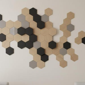 May include: A wall-mounted art installation composed of hexagonal wooden tiles in natural, black, and gray tones. The arrangement creates a modern, geometric design, suitable for home decor. The tiles are arranged in a cluster pattern.