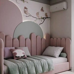 Può includere: Un divano letto imbottito rosa con testiera e pannello laterale smerlati. Il letto presenta una coperta trapuntata verde chiaro, un cuscino bianco, un cuscino con motivo viola e un cuscino quadrato con il disegno di una pecora bianca.