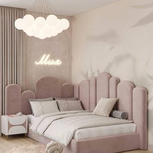 Può includere: Una struttura letto ad angolo rivestita in velluto rosa polvere con un'alta testiera smerlata. Il letto è vestito con biancheria bianca e diversi cuscini decorativi. Un comodino bianco con due aperture circolari è posizionato accanto.