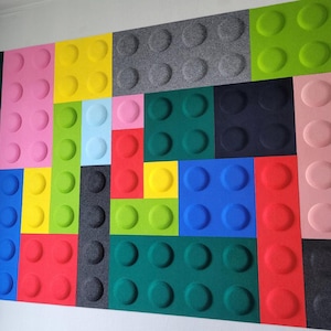 Può includere: Una parete ricoperta di piastrelle di feltro colorate con una varietà di motivi. Ogni piastrella ha un colore e un motivo diverso, tra cui rosa, blu, verde, giallo, rosso e grigio. Le piastrelle sono disposte in modo casuale.