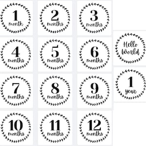Op de afbeelding: Set van 13 witte kaarten met zwarte tekst en bladerkransranden. Elke kaart geeft een maandelijkse of jaarlijkse mijlpaal aan, van 1 maand tot 12 maanden, plus een "Hello World"-kaart.