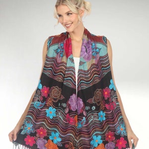 Peut inclure: Un gilet sans manches, noir, à motifs floraux avec une bordure frangée. Le gilet présente un motif coloré avec des fleurs bleues, rouges, oranges, violettes et vertes.