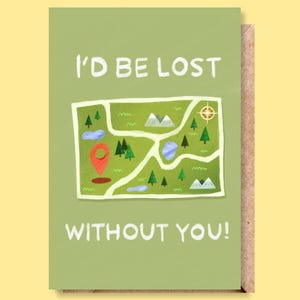 Op de afbeelding: Een wenskaart met een groene achtergrond en de tekst "I'D BE LOST WITHOUT YOU!". De kaart heeft een kaartillustratie met bomen, bergen en een rode locatie-markering. De kaart wordt geleverd met een bruine envelop.