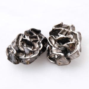 May include: Two silver-toned metal earrings with a textured, organic, and abstract design. The earrings are shaped like a cluster of small, irregular shapes.