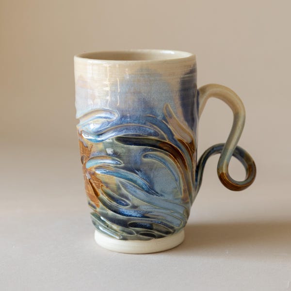 Taza de cerámica tallada a mano inspirada en la playa, con paleta de colores azul y asa única en espiral.