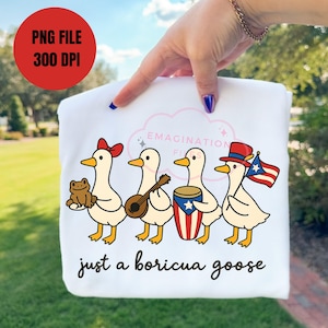 May include: White sweatshirt featuring a cartoon design of four geese, each holding an item: a frog, a lute, a drum, and a Puerto Rican flag. The text "just a boricua goose" is printed below the geese. A red circle with text is in the upper left.