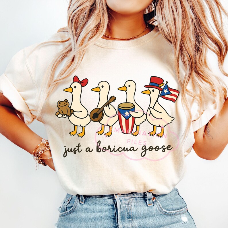 May include: Cream-colored t-shirt featuring a line of cartoon geese, each holding a different item: a frog, a stringed instrument, a drum with a Puerto Rican flag design, and a Puerto Rican flag. The text "just a boricua goose" is below the geese.