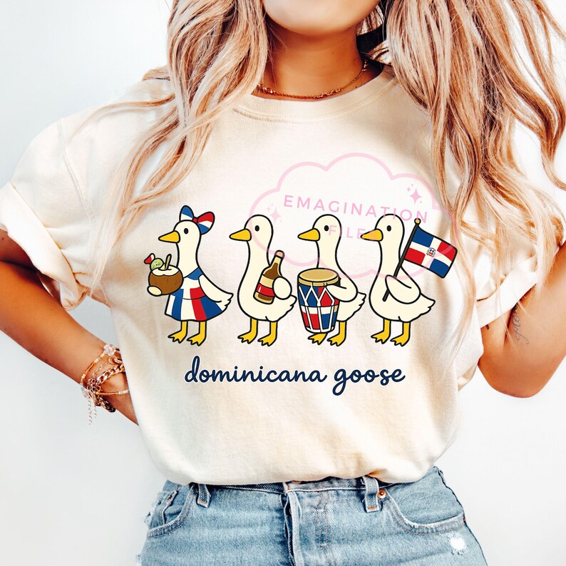 May include: A cream-coloured t-shirt with a cartoon illustration of four geese, each holding items related to the Dominican Republic. The geese are depicted with a cocktail, bottle, drum, and flag. The words "dominicana goose" are written in a script font.