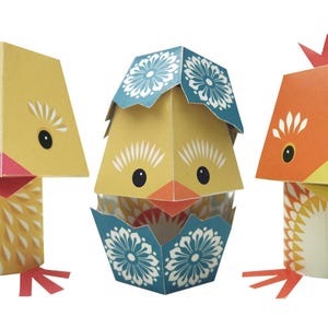 May include: Three paper craft chicks, one yellow chick in an egg with a blue and white patterned shell, one yellow chick standing on its own, and one orange chick standing on its own.