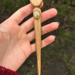 Könnte beinhalten: Ein Holzhaarstab mit einem Halbmond-Design an der Oberseite und einem runden, hellbraunen Edelstein in der Mitte.