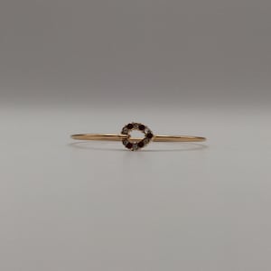 May include: A gold bangle bracelet with a small, heart-shaped charm set with red and clear rhinestones.