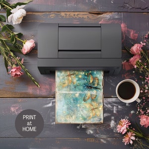 Pu&ograve; includere: Una stampante nera con un foglio di carta che ne esce. La carta presenta un disegno ad acquerello di libellule con accenti dorati e uno sfondo blu. Il testo "PRINT at HOME" &egrave; su un cerchio bianco nell'angolo in basso a sinistra dell'immagine.