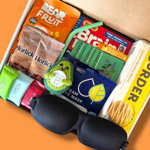 May include: A gift box containing various treats, including Bear Fruit mango snacks, Horlicks chocolate, Clipper tea, and Burt's Bees lip balm. Also features a crocheted avocado and a black eye mask. The avocado has the text "You've totally guac this!"