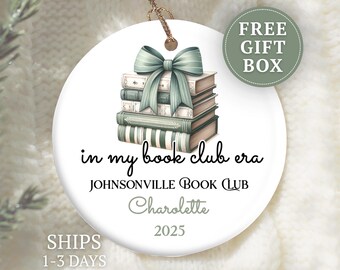 May include: A white ceramic ornament with a stack of books tied with a green bow. The text "in my book club era" and "Johnsonville Book Club" are displayed. The ornament also includes the name "Charolette" and the year "2025".