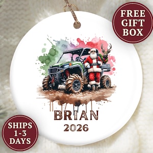 May include: A round white ceramic ornament featuring a watercolor illustration of Santa Claus standing next to a green off-road vehicle with a reindeer in the back. The name BRIAN and the year 2026 are printed in brown text below the illustration.