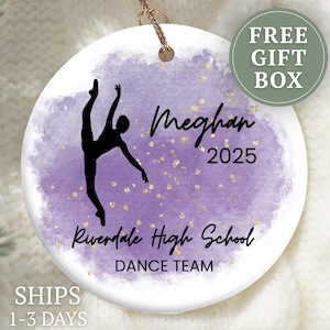 May include: A white ceramic ornament with a purple watercolor background and gold flecks. A black silhouette of a dancer is featured, along with the name "Meghan", the year "2025", and "Riverdale High School DANCE TEAM". Includes a "FREE GIFT BOX" label.