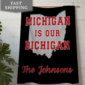 May include: Black wall hanging with the text "MICHIGAN IS OUR BICHIGAN" in red and white, with the shape of the state of Ohio in the center. The name "The Johnsons" is written in red script at the bottom.