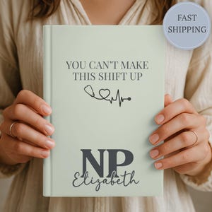 May include: A light green hardcover notebook featuring the dark text "YOU CAN'T MAKE THIS SHIFT UP" above a black stethoscope and heart rate graphic. Below this, the letters "NP" are printed in a large font with the name "Elizabeth" underneath.