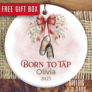 May include: White ceramic ornament with a watercolor design. Features a pink bow, floral arrangement, and tap shoes. Text reads "Born to Tap Olivia 2025". Includes a gold string for hanging.