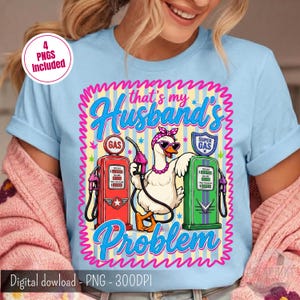 Puede incluir: Una camiseta azul claro con el gráfico de una oca blanca con diadema rosa, gafas de sol en forma de corazón y collar de perlas. La oca está entre un surtidor de gasolina rojo y uno verde. Texto: that's my Husband's Problem.