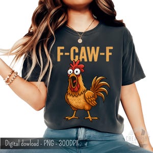 Puede incluir: Camiseta gris oscuro con un gallo de dibujos animados y el texto "F-CAW-F" en dorado. El gallo es marrón con cresta y barbilla rojas. La camiseta la lleva una persona. Prenda de vestir informal.