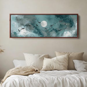 Può includere: Un'opera d'arte incorniciata che raffigura una scena notturna con una luna piena e uccelli in volo. L'opera presenta una tavolozza di colori verde acqua e bianco, con una cornice marrone scuro. L'arte è esposta sopra un letto con biancheria da letto bianca.