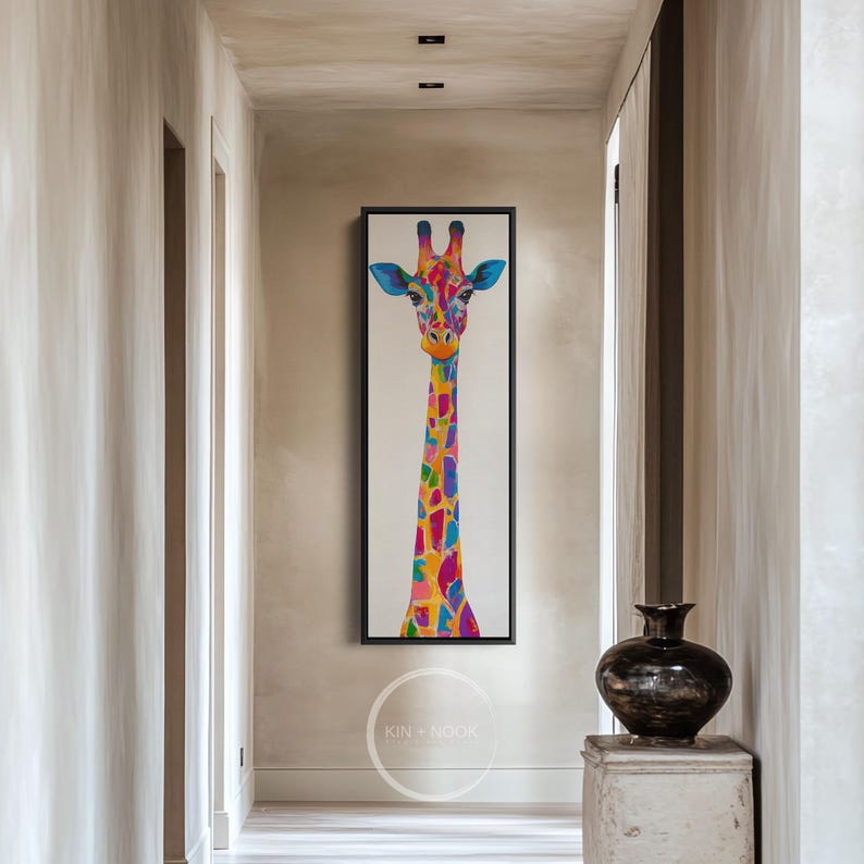 May include: A vibrant giraffe painting in a black frame. The giraffe's long neck is adorned with a patchwork of bright colours, including blue, pink, yellow, and orange. The artwork is displayed in a hallway.