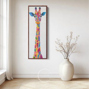 May include: A vibrant painting of a giraffe, framed in dark wood, against a white backdrop. The giraffe features a colourful pattern of blues, pinks, yellows, and oranges. The artwork is displayed on a white wall, with a vase of dried flowers in the foreground.