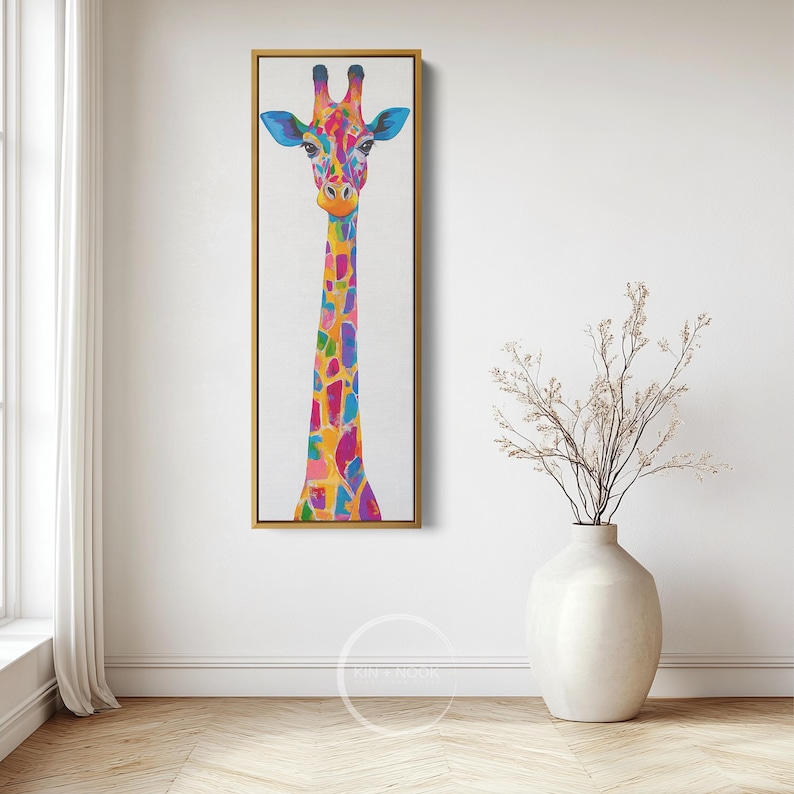 May include: A vibrant painting of a giraffe, framed in gold, against a white backdrop. The giraffe features a colourful pattern of blues, pinks, yellows, and oranges. The artwork is displayed in a room with a vase of dried flowers.