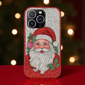 May include: A bedazzled phone case featuring a Santa Claus design. The case is covered in red and white rhinestones, with a detailed image of Santa's face, hat, and beard. The case is designed to fit a smartphone.