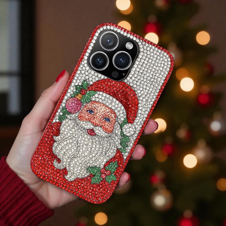 May include: A bedazzled phone case featuring a Santa Claus design. The case has a red border and a Santa illustration with a white beard and red hat. The background is covered in white and red crystals, creating a festive holiday theme.