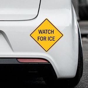 K&ouml;nnte beinhalten: Ein gelber, rautenf&ouml;rmiger Aufkleber mit schwarzem Rand und den Worten "WATCH FOR ICE" in schwarzer Schrift. Der Aufkleber ist am Heck eines wei&szlig;en Fahrzeugs in der N&auml;he des R&uuml;cklichts angebracht.