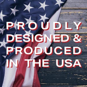 K&ouml;nnte beinhalten: Eine amerikanische Flagge liegt auf einer dunklen Holzoberfl&auml;che. Das blaue Feld der Flagge mit wei&szlig;en Sternen und roten und wei&szlig;en Streifen ist zu sehen. Fettgedruckter wei&szlig;er Text mit roten Umrissen lautet "PROUDLY DESIGNED & PRODUCED IN THE USA."