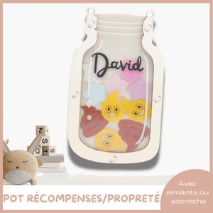 Peut inclure: Un tableau de récompenses en forme de pot en bois blanc avec le nom "David" en écriture noire. Le pot contient des jetons colorés en forme d'étoiles et d'emojis. Le texte "POT RÉCOMPENSES/PROPRETÉ" est en bas.