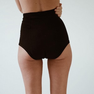 Puede incluir: Ropa interior negra de cintura alta con un acabado liso y sin costuras.