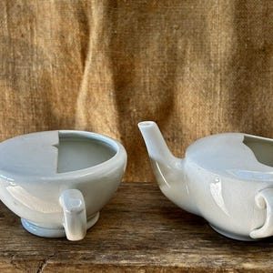 May include: Two white ceramic enema jugs with a spout and a handle. The jugs have a smooth, glossy finish.