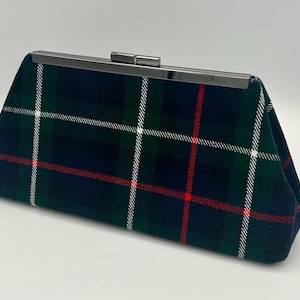 May include: A rectangular clutch with a plaid pattern in navy, green, red, and white. The clutch has a silver-colored metal clasp closure. The fabric appears to be a woven material.
