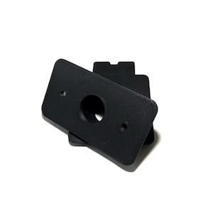 May include: Black rectangular plastic plates with a circular hole and two smaller holes. The plates are stacked on a white background. The plates have a matte finish.