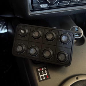 May include: A black rectangular switch panel featuring eight circular buttons arranged in two rows of four. The top-left button displays a small logo with the text LINCE. Below the panel, a gear shift pattern sticker shows the text RAZO.