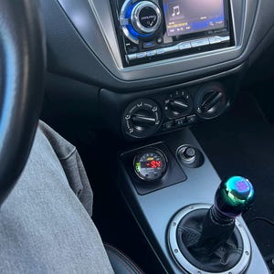 May include: The interior of a car with a black and silver dashboard. The car has a digital gauge that reads 18.4, a gear shifter with a green and purple knob, and a car stereo with a screen that says "No USB Device".