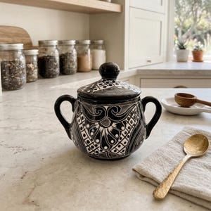 May include: A set of three ceramic mugs with a speckled, cream-colored glaze. Each mug features a different hand-painted design: a blue and green leaf, a yellow flower, and a red berry. The mugs have a simple, rounded shape.