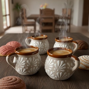 May include: Four ceramic mugs with coffee, brown rims, and handles, decorated with a white floral pattern, sit on a wooden table. Several concha pastries, some pink and some brown, are also on the table. Steam rises from the coffee.